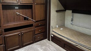 A compact room with a bunk bed, built-in wooden cabinets, and a TV in a cabinet. - Spacious Lakeside Travel Trailer: Ultimate Comfort Awaits (Bridgeport)