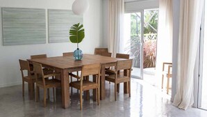 A spacious dining area with a wooden table and chairs, a vase with a plant, and a large window with curtains. - Gorgeous Villa With Views (Sant Josep de sa Talaia)