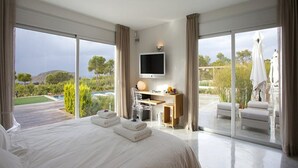 A spacious bedroom with a large bed, a desk, and a TV. It has a sliding glass door leading to a balcony with outdoor furniture. - Gorgeous Villa With Views (Sant Josep de sa Talaia)