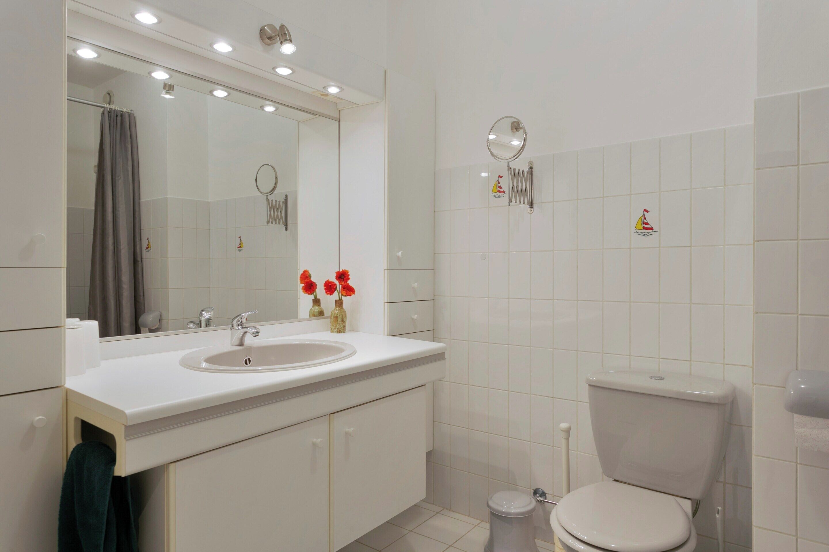 A modern bathroom with a white sink, mirror, and toilet.