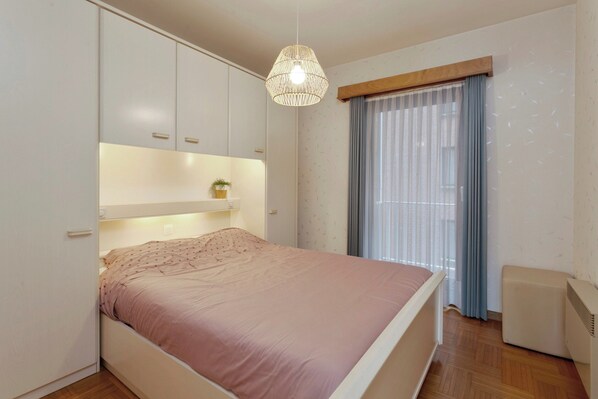 A bedroom with a bed, built-in wardrobe, bedside table, and a hanging light fixture. - Apartment With Terrace for 5 People (Blankenberge)
