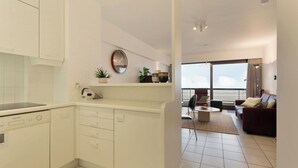 Una cucina moderna con mobili bianchi, lavastoviglie e un'ampia finestra con vista su un balcone.