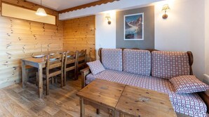 A cozy room with a wooden dining table, chairs, a patterned sofa, and a painting on the wall. - 40m from ski slopes, 1st floor, fitness, swimming pool, sauna, balcony, tv, ski locker, 35m² (Les Orres)