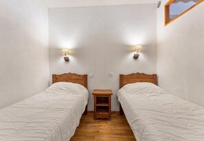 Une petite chambre propre, avec deux lits simples, une table de chevet en bois et des lampes fixées au mur.