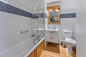A modern bathroom with a glass-enclosed shower, a wooden vanity, a white toilet, and a mirror above the sink.