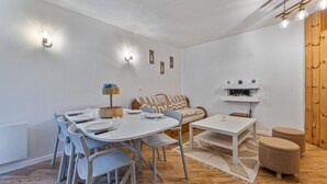 A modern, well-lit dining area with a round table, chairs, and a wooden sideboard. - 40m from ski slopes, floor -3, view ski slopes, fitness, swimming pool, sauna, balcony, tv (Les Orres)