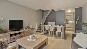 A modern living room with a flat-screen TV, wooden furniture, a staircase, and a kitchen area. - Duplex in Blankenberge Steps From Seafront (Blankenberge)