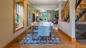 A spacious dining area with a long wooden table, cushioned chairs, and a patterned rug.