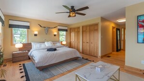 A bedroom with a bed, bedside tables, a ceiling fan, a nightstand, a window, and a door.