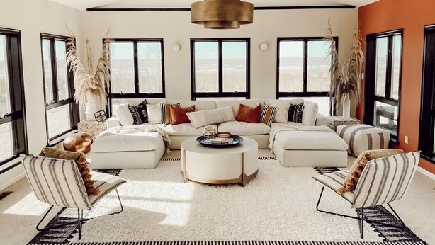 A spacious living room with a high ceiling, large windows, and a central seating area with a coffee table.