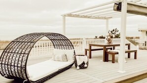 A beachside deck with a hanging chair, a table, and a covered seating area.