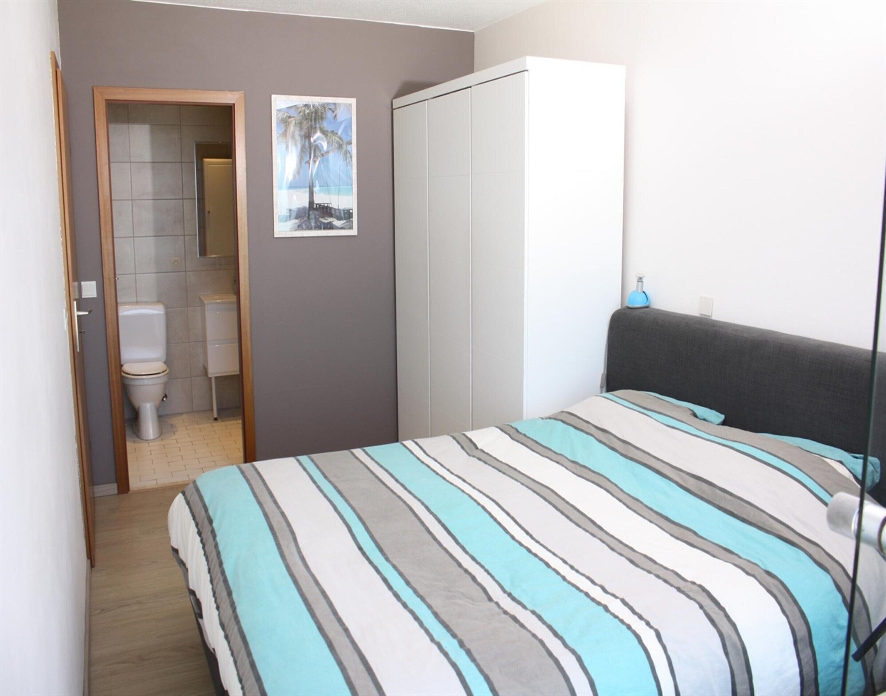 Une chambre à coucher comprenant un lit, une armoire, une salle de bain avec des toilettes et un tableau encadré au mur.