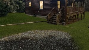 Una cabaña de troncos con un porche y escaleras, rodeada de césped y árboles.