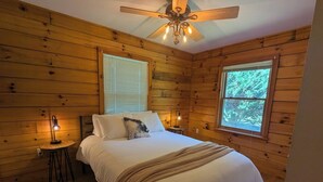 Un dormitorio con detalles de madera, una cama con ropa de cama blanca, una lámpara de noche y un ventilador de techo.