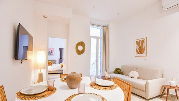 A dining area with a round table set for four, a sofa, and a TV mounted on the wall.