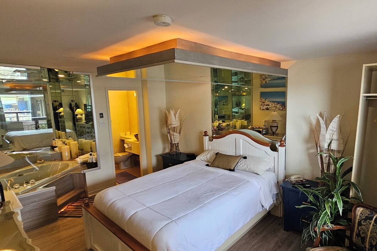 Une chambre d’hôtel moderne dotée d’un grand lit, d’un coin salon avec une table et des chaises, d’une salle de bain avec baignoire et d’une armoire avec des vêtements suspendus.