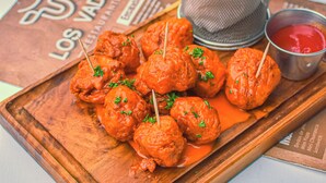 A wooden board with skewered meatballs garnished with parsley, a basket of French fries, and a small bowl of ketchup. - Los Vados Hotel  (Managua)