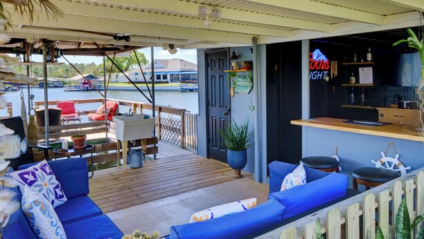 A covered outdoor seating area with blue cushioned sofas and a wooden deck.