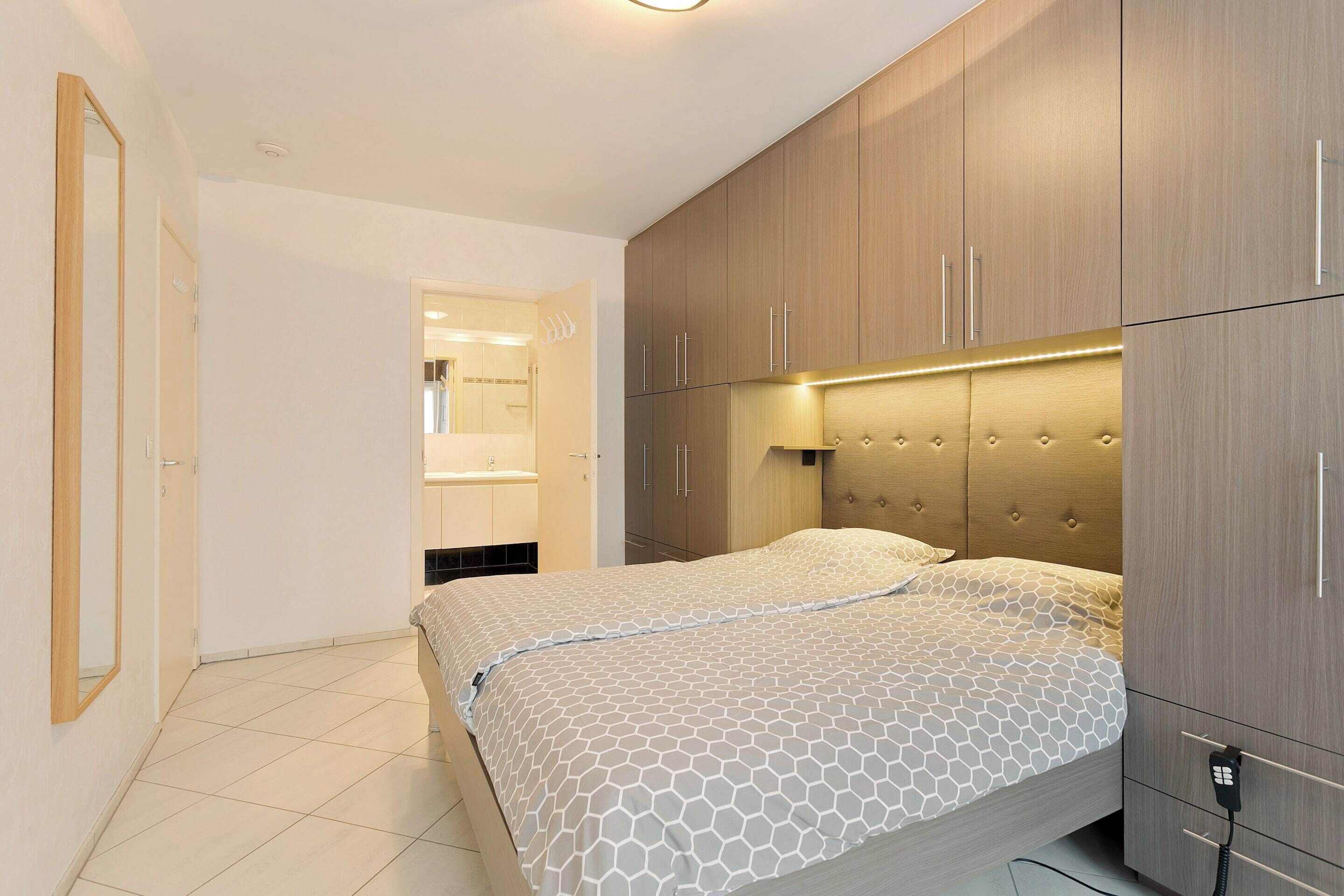 A bedroom with a bed, wooden wardrobe, and a bathroom visible through an open door.