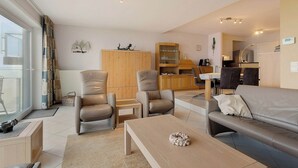Ein modernes Wohnzimmer mit einer Couch, zwei Sesseln, einem Couchtisch und einem Essbereich im Hintergrund.