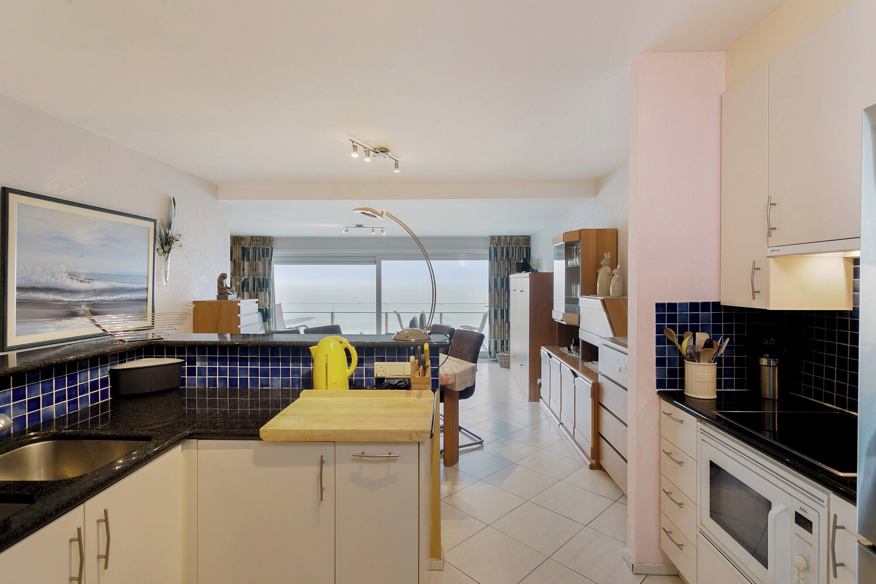 A modern kitchen with a dining area, large windows, and a view of the sea.