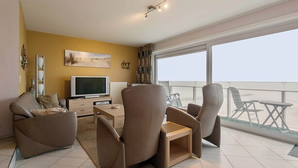 Una sala de estar moderna con un televisor de pantalla plana, dos sofás, una mesa de centro y un balcón con mobiliario exterior.