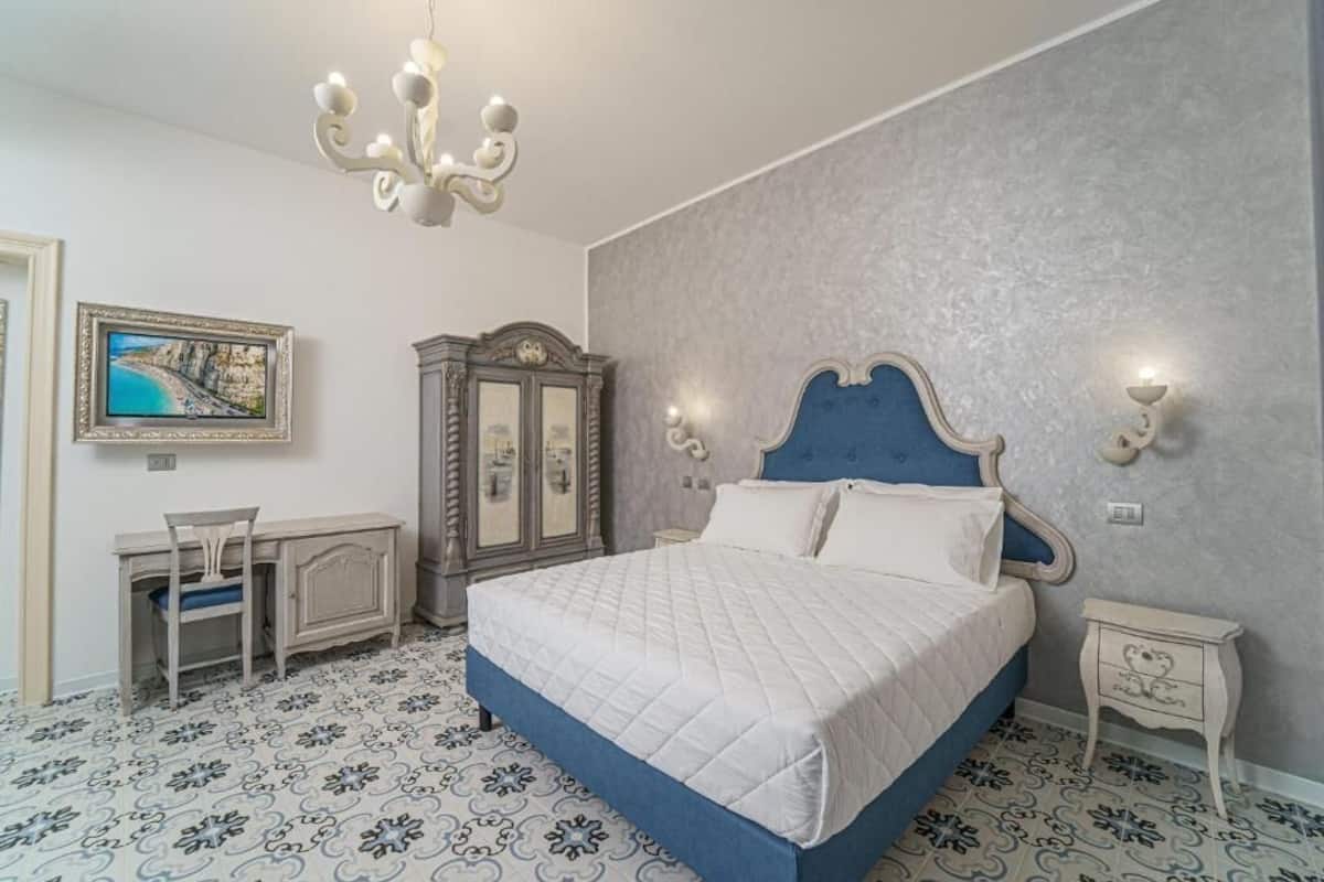 A bedroom with a bed, a desk, a chair, a wardrobe, and a wall-mounted TV.