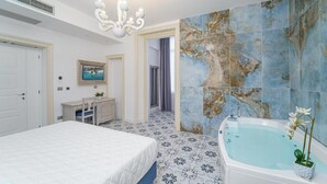 Un dormitorio con una cama grande, un tocador con espejo y una bañera con un jarrón de flores.