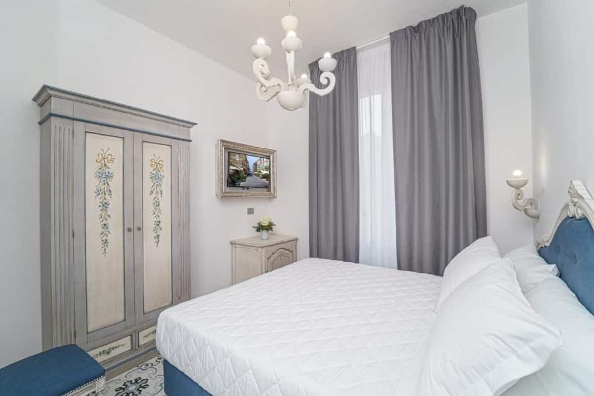 A bedroom with a bed, a wardrobe, a chandelier, a mirror, and curtains.