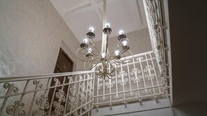 Un candelabro con múltiples luces colgando del techo, una barandilla metálica blanca con diseños decorativos y una puerta al fondo.