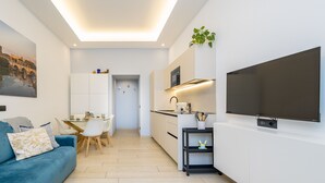 A modern living room with a blue sofa, a dining area with a white table and chairs, a kitchen with white cabinets and a black TV on the wall. - Charming 1-bedroom apt. with AC, WiFi, lift.  in central Roma, close to Colosseo (Roma)