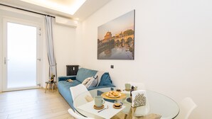 A modern living room with a glass dining table, white chairs, a blue sofa, and a large framed picture on the wall. - Charming 1-bedroom apt. with AC, WiFi, lift.  in central Roma, close to Colosseo (Roma)