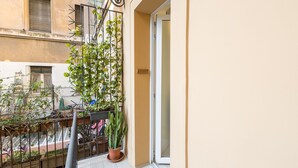 A balcony with a potted cactus, a metal trellis with climbing plants, and a door leading to a room. - Charming 1-bedroom apt. with AC, WiFi, lift.  in central Roma, close to Colosseo (Roma)