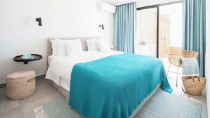 Een moderne hotelkamer met een bed, een klein bijzettafeltje, een rond poefje, een balkon met een stoel, en uitzicht op de omgeving.
