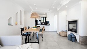 Een moderne woonkamer met een eethoek, een keuken op de achtergrond en een open haard.
