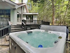 Un jacuzzi en una terraza de madera con una casa al fondo.