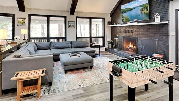 A modern living room with a sofa, a foosball table, a fireplace, and a TV mounted on the wall. - Koi at the Lake by Taylor Made Deep Creek (Oakland)