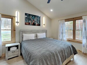A bedroom with a bed, nightstands, a painting, and windows. - Majestic Manor by Taylor Made Deep Creek (McHenry)