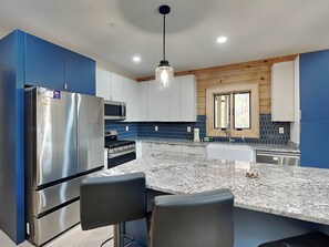 A modern kitchen with stainless steel appliances, a granite countertop, and blue cabinetry. - Majestic Manor by Taylor Made Deep Creek (McHenry)