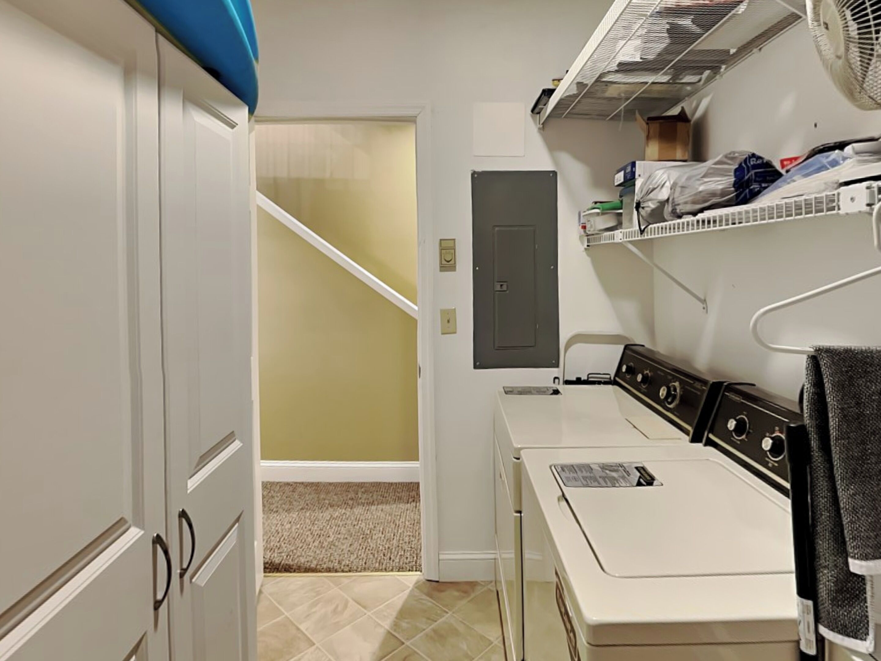 A laundry room with a dryer, a washing machine, and a utility room with shelves and a door.
