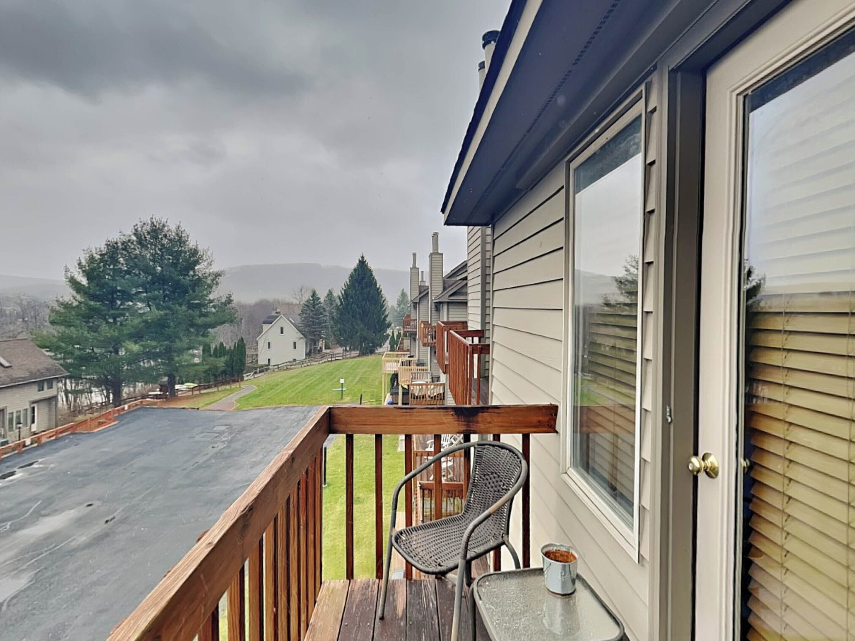 A balcony with a wooden railing, a table, and a chair.