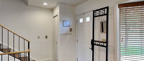 A hallway with a wooden staircase, a door with a mirror, and a window with blinds.