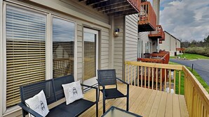 A deck with a sofa and chairs, a table, and a view of a road and greenery. - Happy Time by Taylor Made Deep Creek (McHenry)