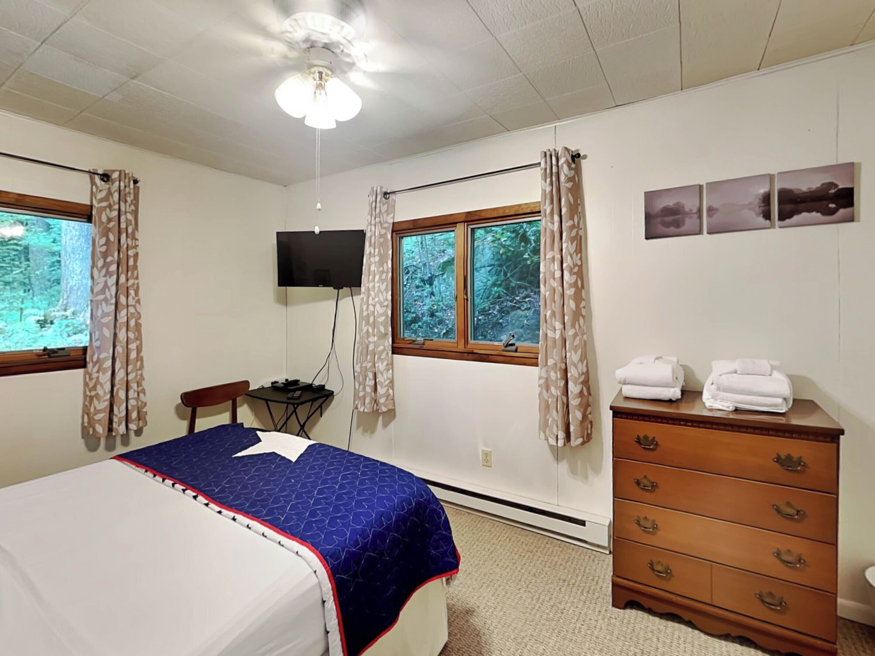 A bedroom with a bed, a dresser, a TV, and a window with curtains.