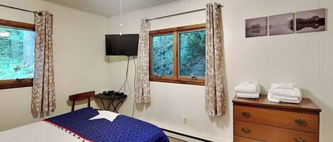 A bedroom with a bed, a dresser, a TV, and a window with curtains.