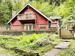 A red cabin with a balcony, surrounded by lush greenery. - An Apple Away by Taylor Made Deep Creek (Oakland)