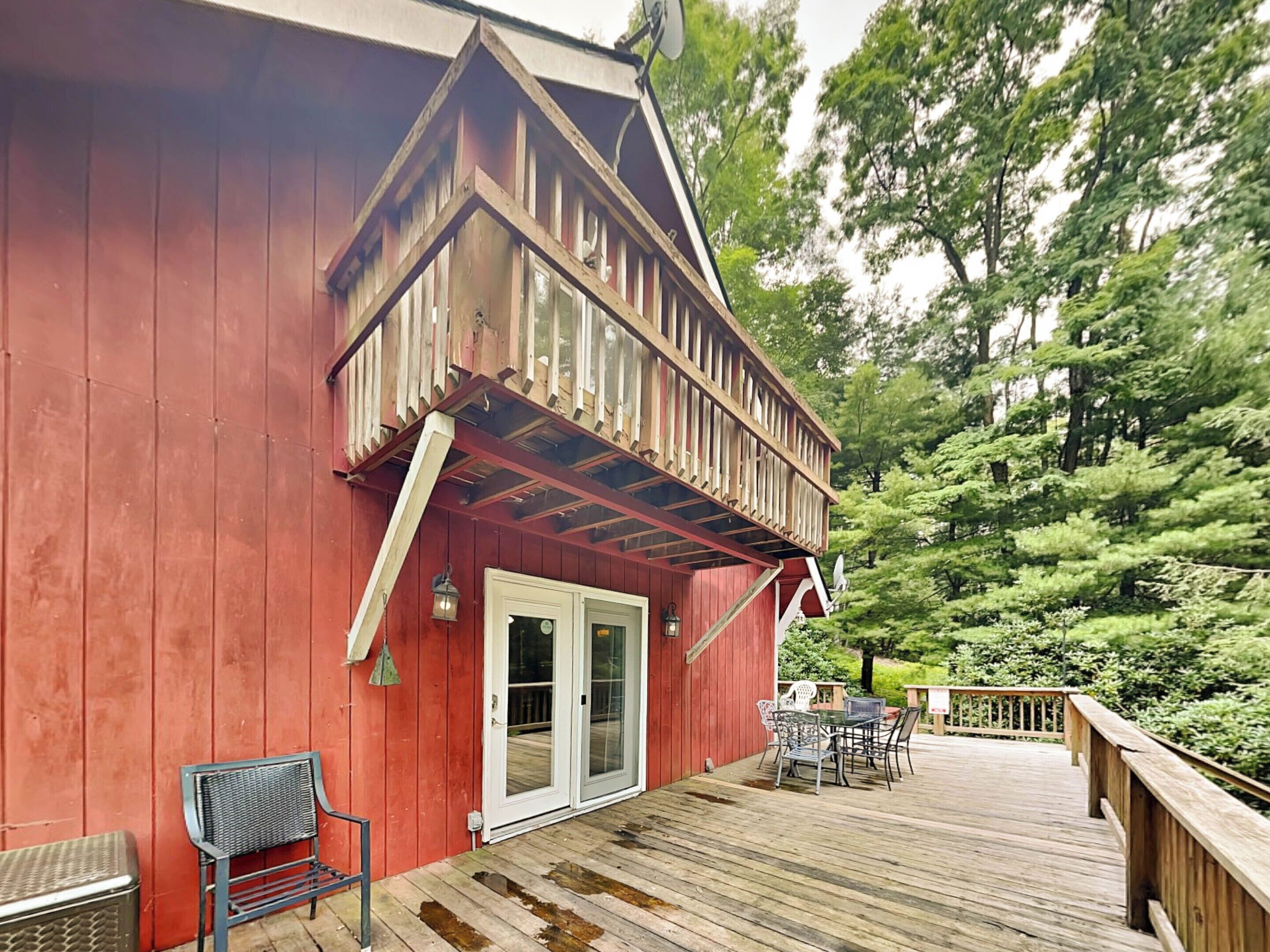 Een rood houten gebouw met balkon, een deur en een tafel met stoelen.