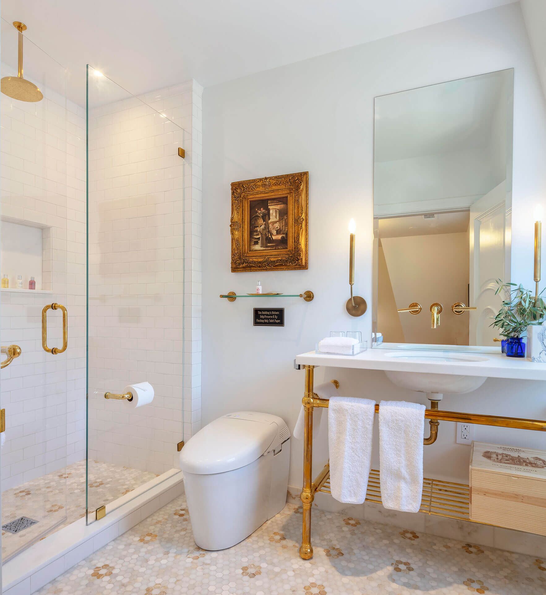 A modern bathroom with a glass-enclosed shower, a white toilet, a vanity with a large mirror, and a gold-colored towel rack.