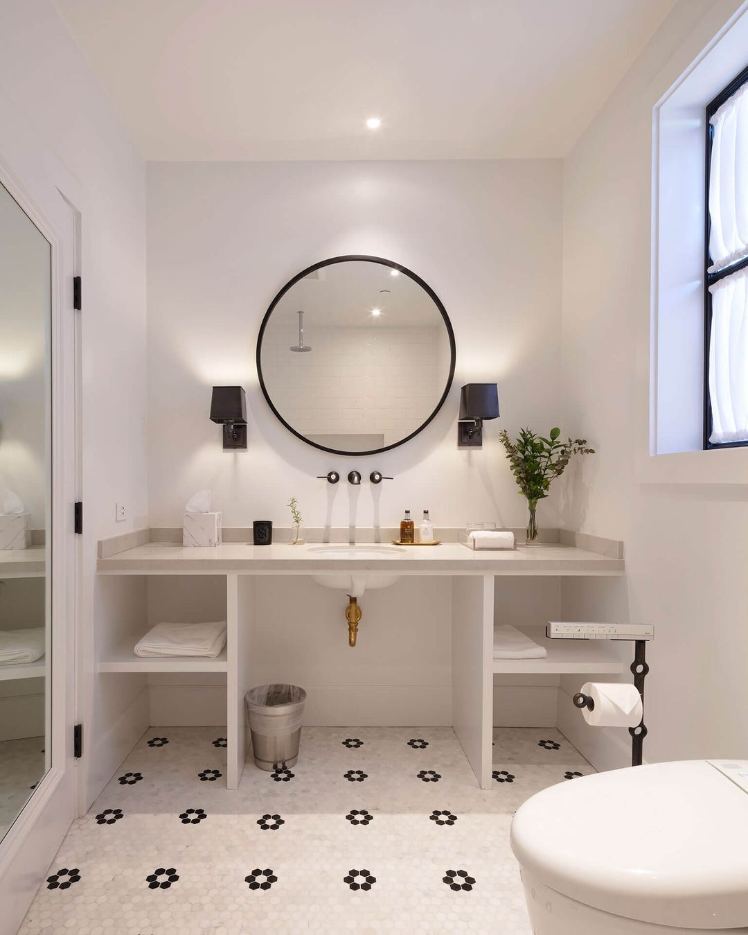 Een moderne badkamer met een ronde spiegel, een witte wastafel en een toilet.