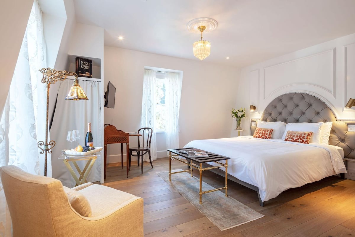 A bedroom with a large bed, a desk, a chair, and a chandelier.